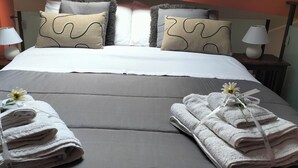A neatly made bed with grey bedding and two pillows, a bedside table with a lamp, and two towels with a flower on each.