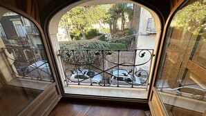 A room with a large arched window overlooking a courtyard with a metal railing and parked cars.