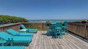 A wooden deck with turquoise lounge chairs and tables overlooking the ocean.