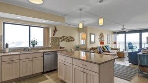 A spacious kitchen with a large island, a dishwasher, and a view to the outside. There is a dining area with a blue chair and a table.