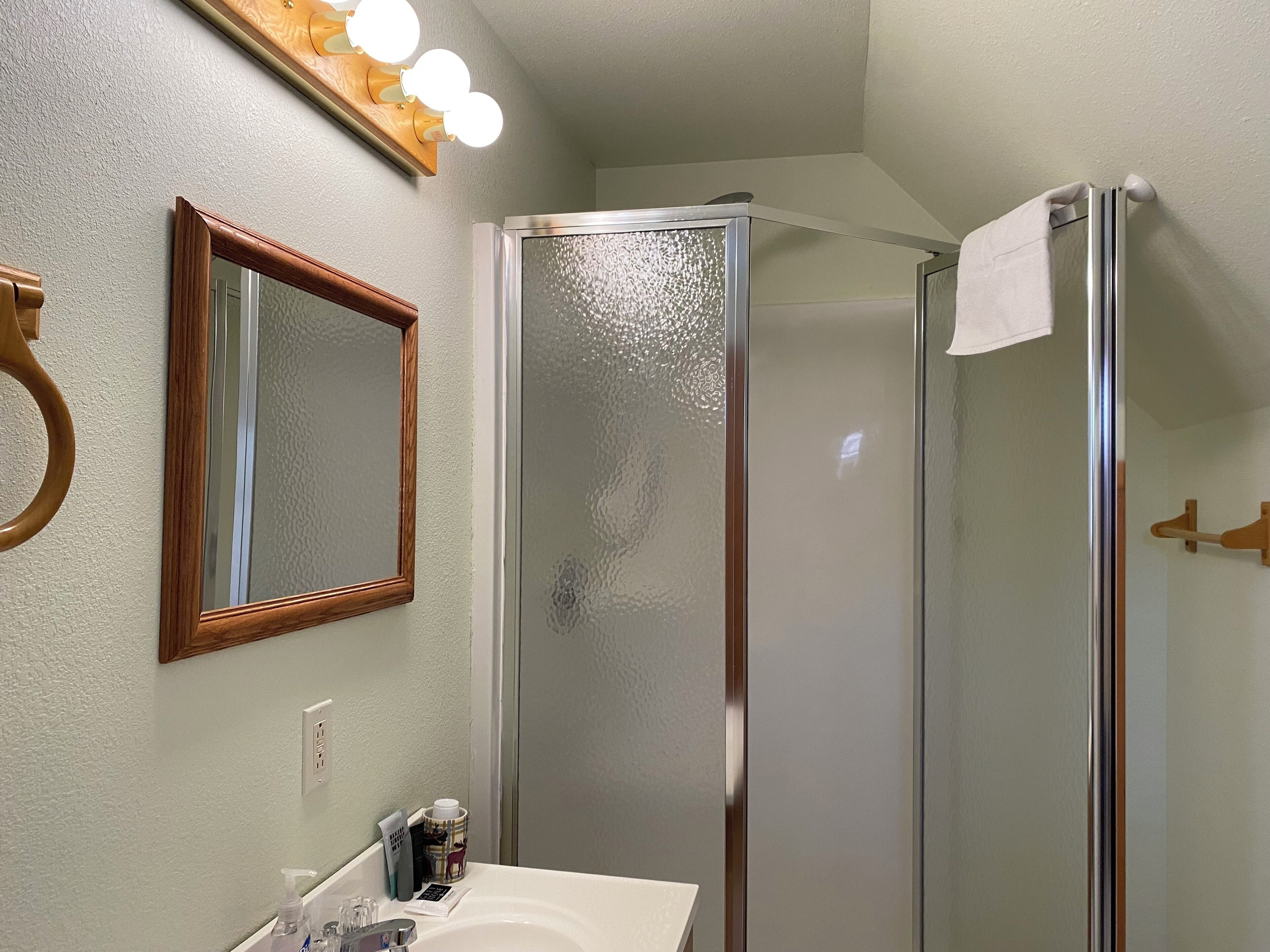 A bathroom with a glass shower enclosure, a wooden-framed mirror, and a sink with toiletries.