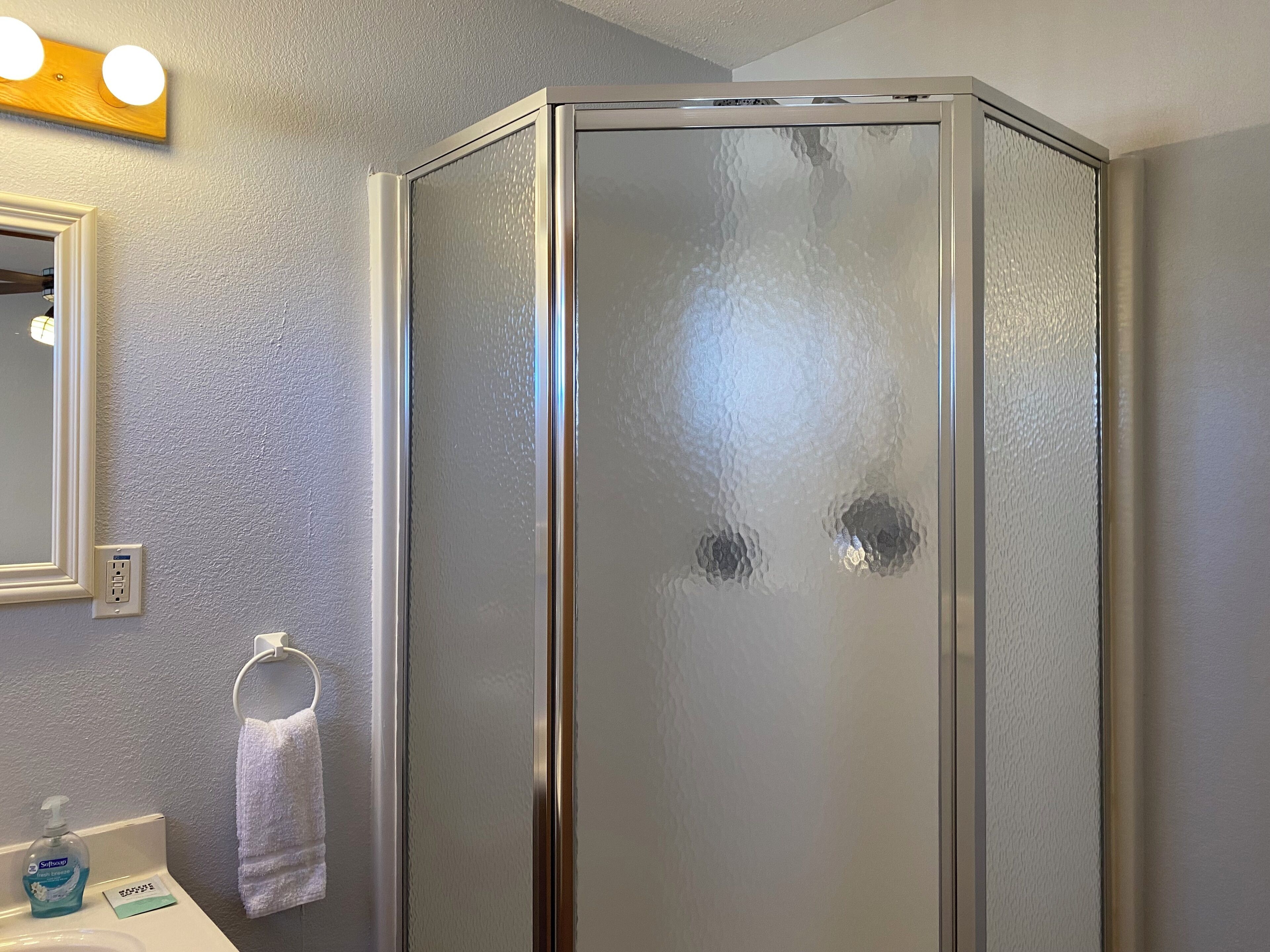 Une salle de bain équipée d’une douche, d’un lavabo, d’un miroir et d’un porte-serviettes.