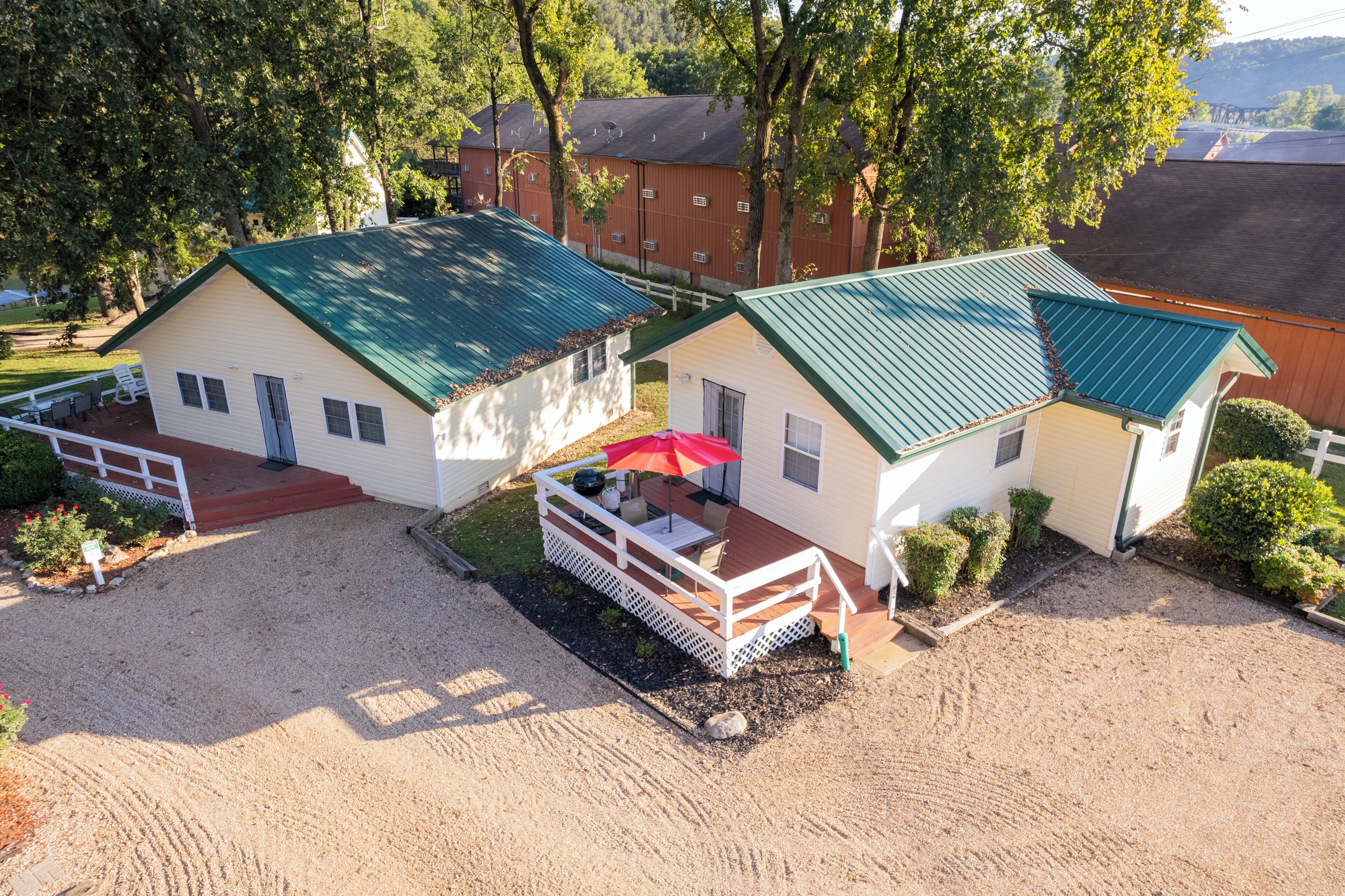 A two-story building with a green roof, a covered patio with a red umbrella, and a gravel driveway.