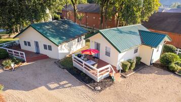 A two-story building with a green roof, a covered patio with a red umbrella, and a gravel driveway.