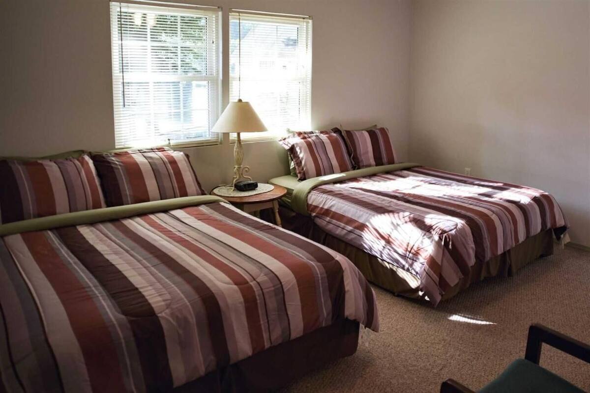Una habitación con dos camas, una mesita redonda con lámpara y una ventana con persianas.