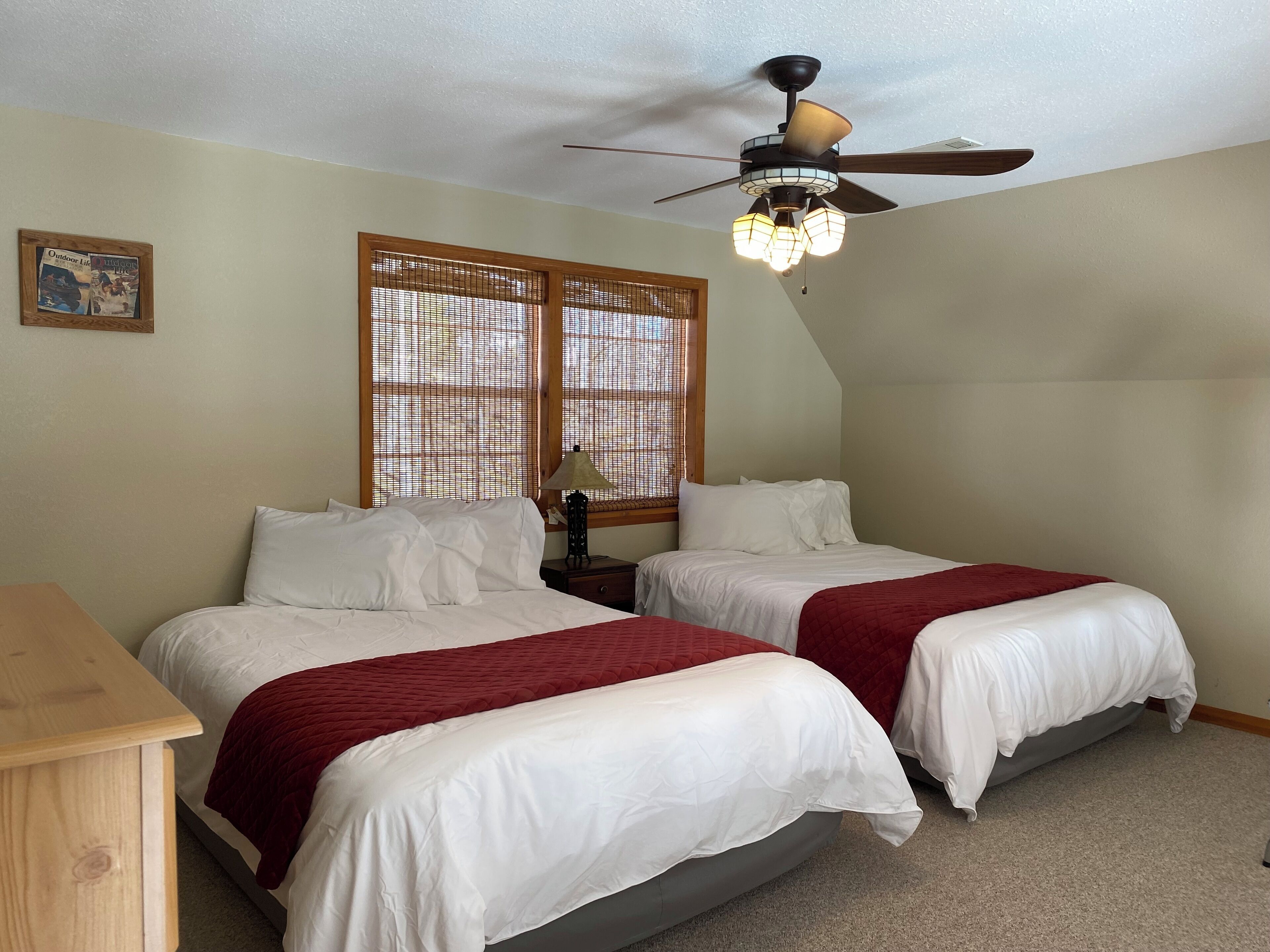 A bedroom with two beds, a ceiling fan, and a window with blinds.