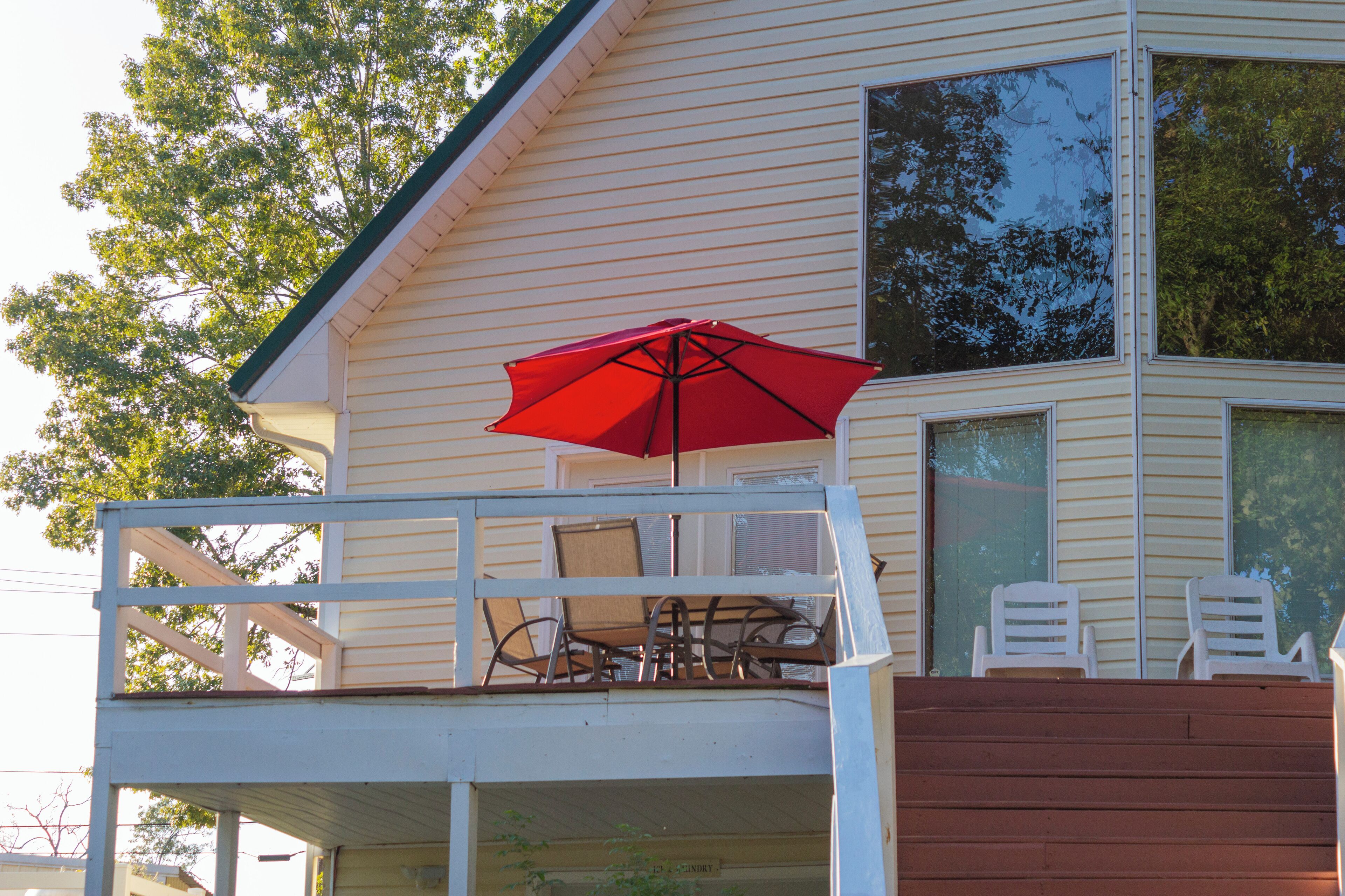 A house with a balcony, a red umbrella, and two white chairs.