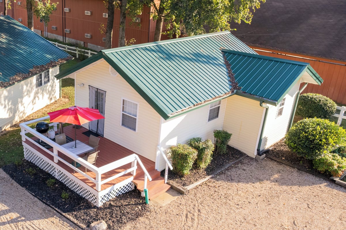 Una casa de dos pisos con techo verde, un patio cubierto con un paraguas rojo y un pequeño jardín.