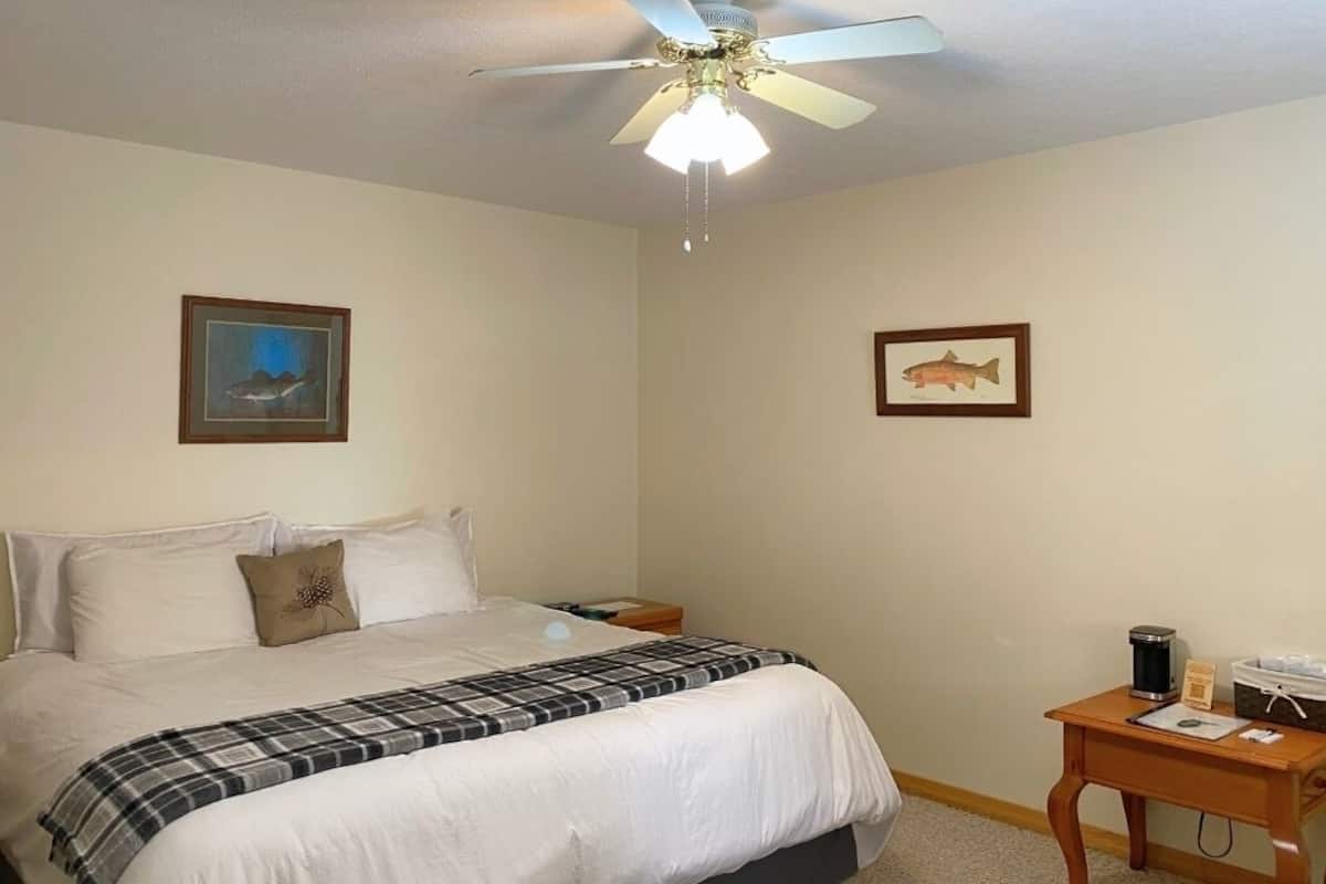 Un dormitorio con cama, mesita de noche, ventilador de techo y dos cuadros en la pared.