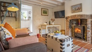 Een gezellige woonkamer met een open haard, een boekenplank en een aan de muur bevestigde televisie.