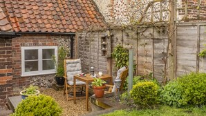 Een gezellig terras met een houten tafel en stoelen, omgeven door plantenpotten en een bakstenen muur.