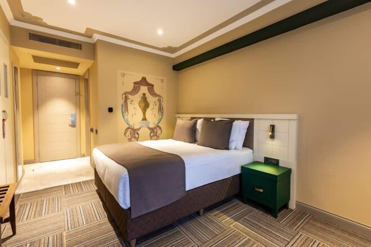 A hotel room with a bed, a bedside table, a wall-mounted light, and a door.
