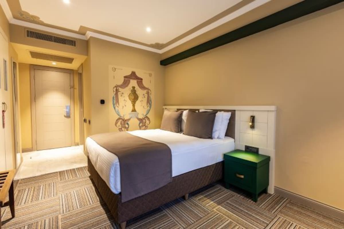Een hotelkamer met een bed, nachtkastje, wandlamp en een deur.