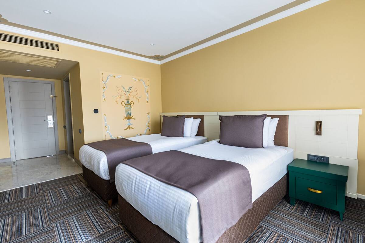 A hotel room with two beds, a green nightstand, and a wall mural.
