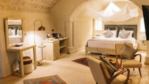 A cozy bedroom with a stone ceiling, a large bed with a canopy, a bedside table, a chair, and a desk with a lamp. - Zemi Hotel Cappadocia (Nevsehir)