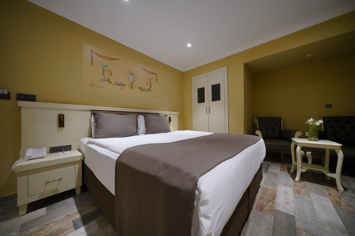 A hotel room with a large bed, a bedside table, a nightstand, a sofa, and a small table with a vase.