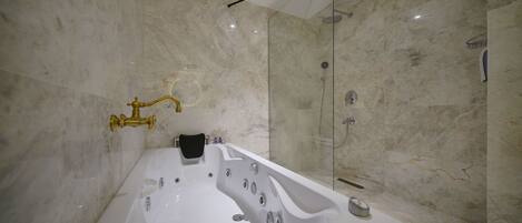 Un baño moderno con una bañera amplia, una ducha con cerramiento de vidrio y paredes de mármol.