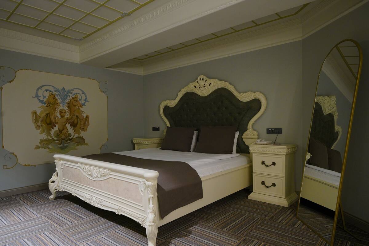 A bedroom with a large bed, two bedside tables, a mirror, and a decorative wall piece.
