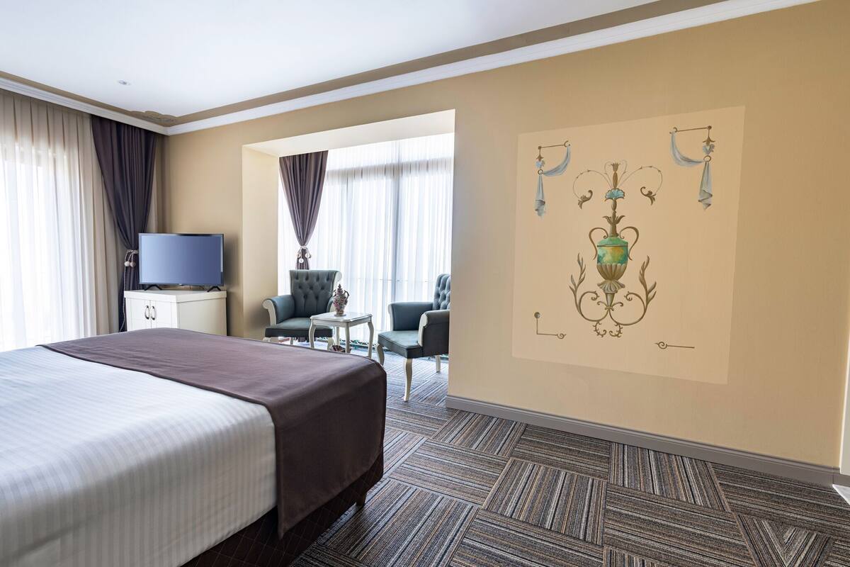 A hotel room with a large bed, a television, a desk, and a chair.