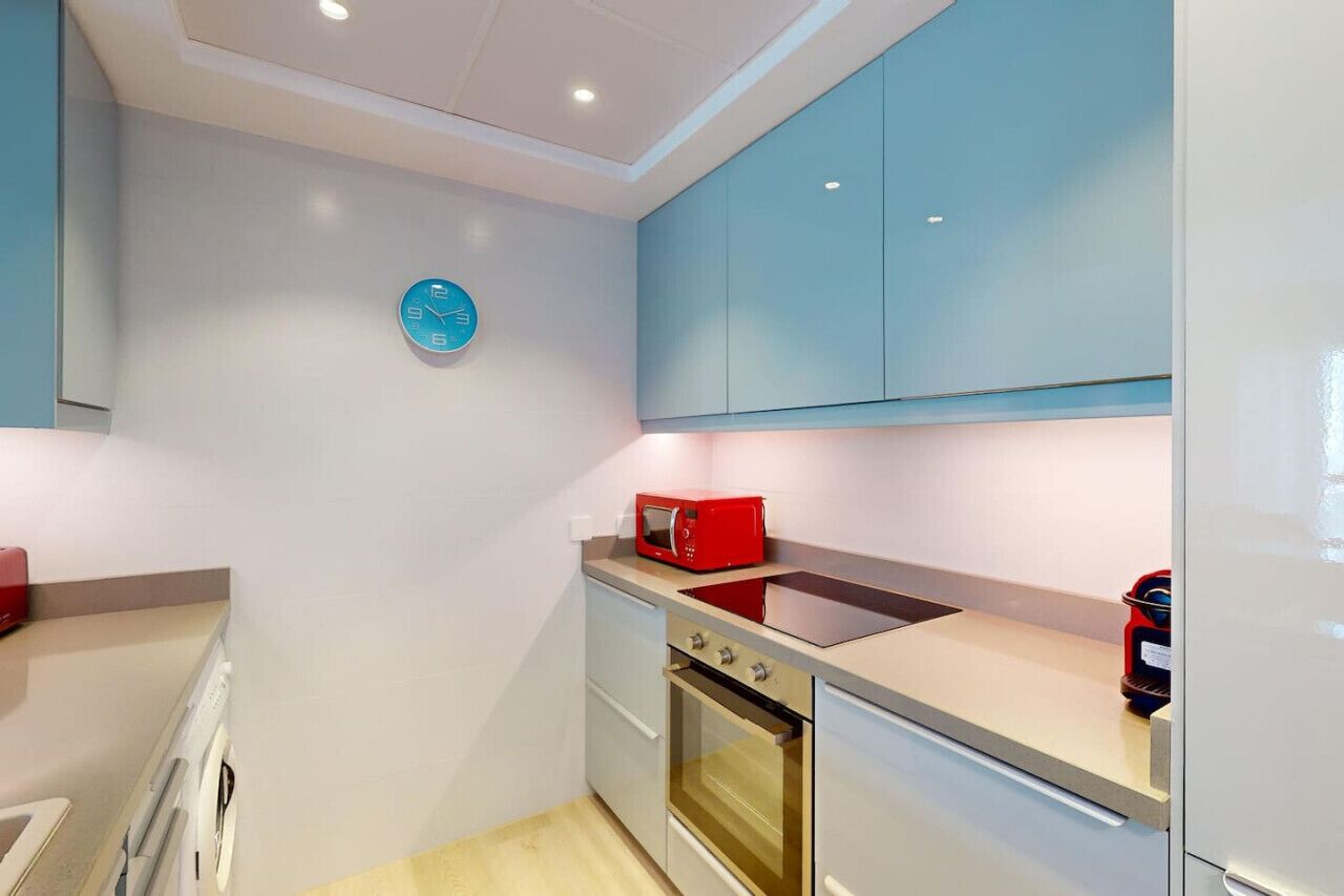 A compact kitchen with light blue cabinets, a red microwave, and a built-in oven.