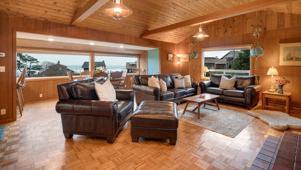 Ein geräumiges Wohnzimmer mit Holzböden und -decke, Ledersofas und großen Fenstern mit Meerblick.