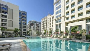 Une piscine entourée de bâtiments modernes, avec des chaises longues et des parasols.