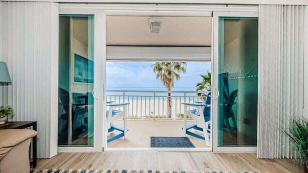 Ein Zimmer mit einer Schiebetür, die auf einen Balkon mit Meer- und Palmenblick führt.
