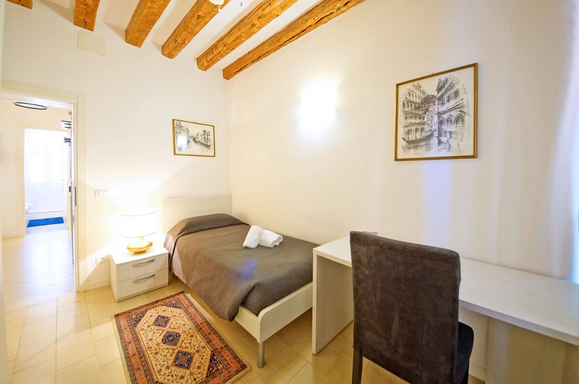 A bedroom with a bed, bedside table, lamp, chair, and two framed pictures on the wall.