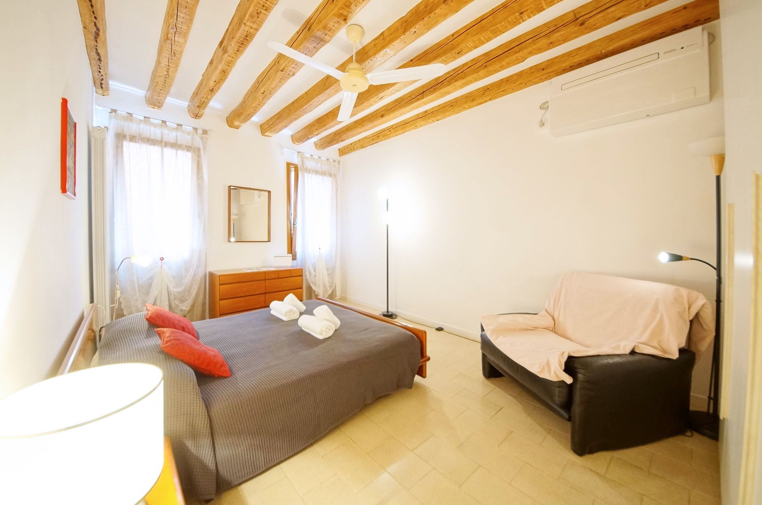 A bedroom with a bed, a sofa, a bedside table, a lamp, and a ceiling fan.