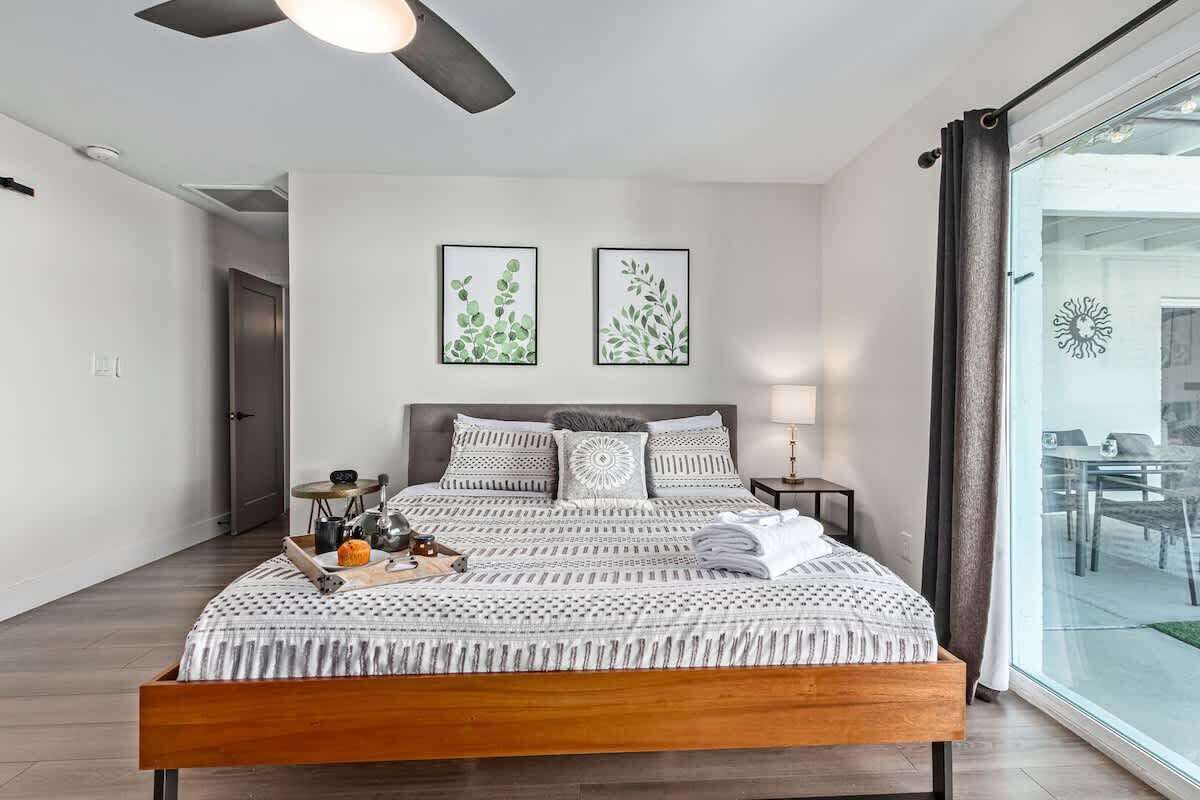 A modern bedroom with a wooden bed, a ceiling fan, and two framed botanical prints on the wall.