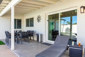 Een terras buiten met een tafel, stoelen en een lounge fauteuil, plus een vuilnisbak.