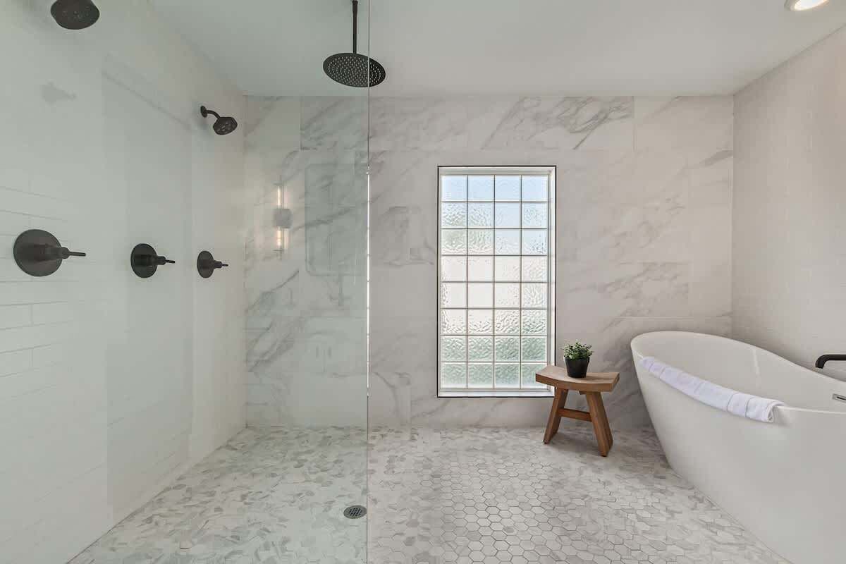 Une salle de bain moderne avec une douche à parois de verre, une baignoire sur pieds et un petit tabouret en bois sur lequel est posée une plante en pot.
