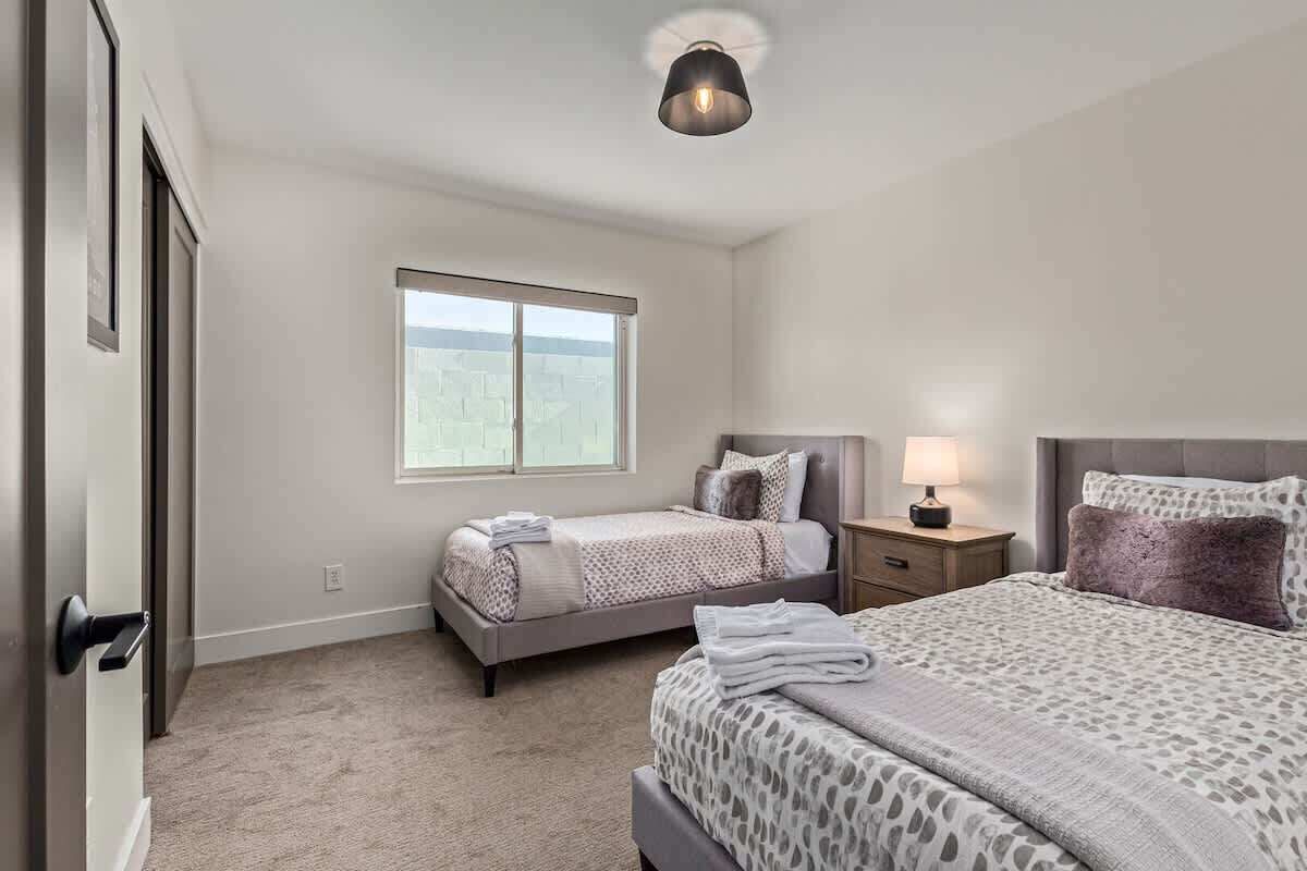 Een slaapkamer met twee bedden, een raam, een nachtkastje met een lamp en een deur.