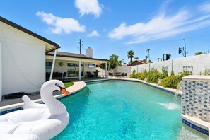 A swimming pool with a swan float, a covered patio, and a view of a residential area.
