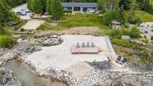 A lakeside property with a deck, outdoor seating, and a stone fire pit.