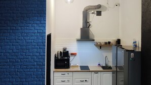 A compact kitchen with a blue brick wall, a hanging light fixture, a built-in oven, and a refrigerator. - VIKI Kazimierz (Kraków)
