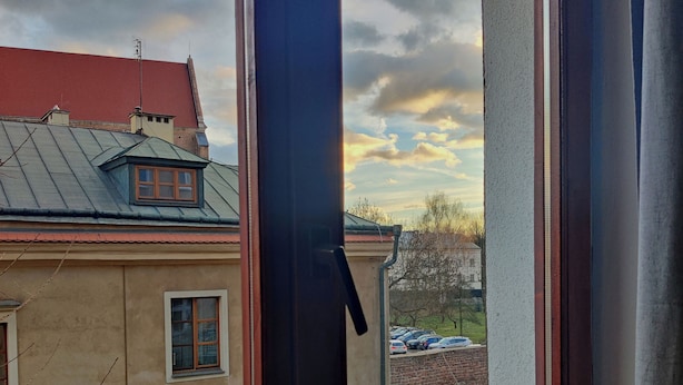 A room with a large window overlooking a residential area, a door, and a view of a building with a red roof. - VIKI Kazimierz (Kraków)