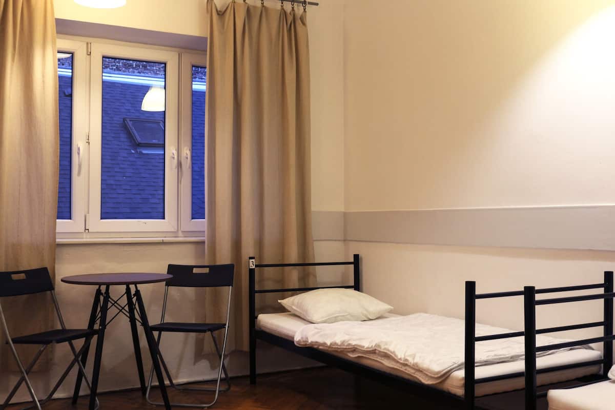 A small room with a single bed, a table, two chairs, and a window with curtains.