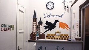 A reception desk with a clock, a 'Welcome!' sign, and a 'Check In' and 'Check Out' sign. - VIKI Kazimierz (Kraków)
