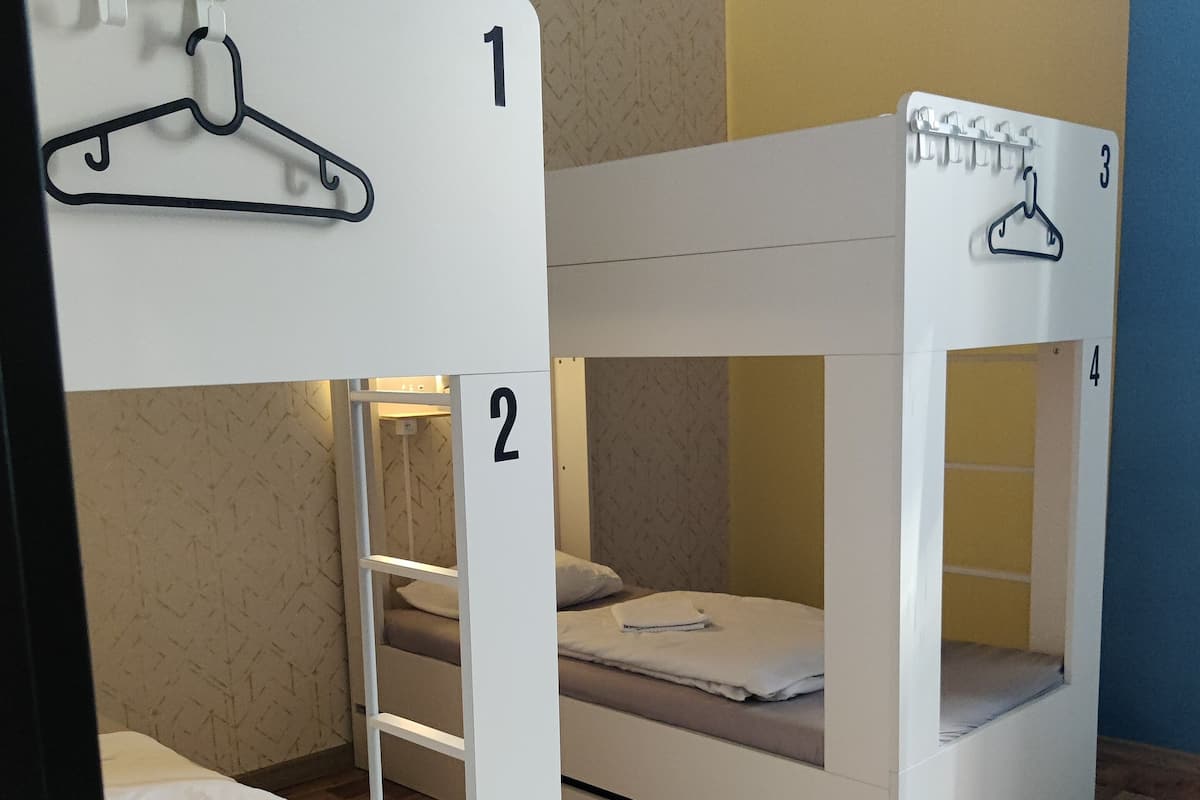 A room with bunk beds labeled 1, 2, 3, and 4, wooden flooring, and a wall with a geometric pattern.
