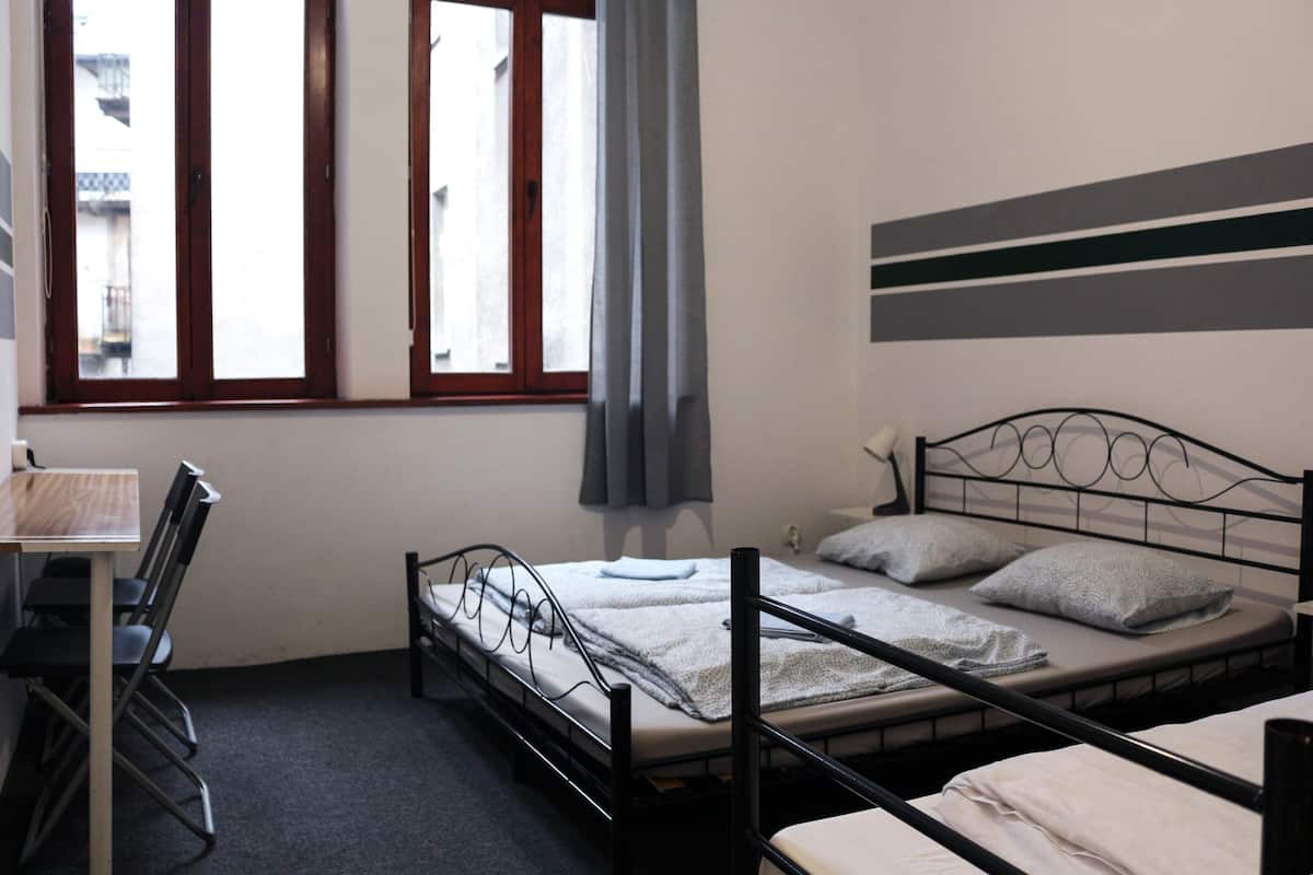 A room with a bed, a desk, and a chair. There is a window with curtains.