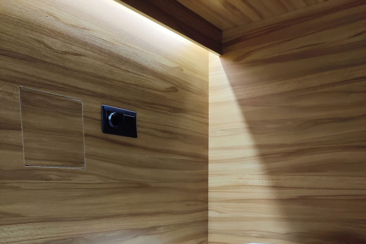 A single bed with white bedding in a room with wooden panel walls and a small black object on the wall.