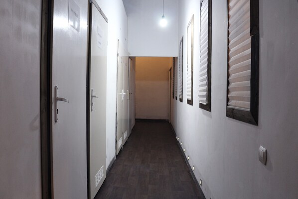 Un couloir étroit, avec des portes sur le côté gauche et des stores aux fenêtres sur le côté droit.