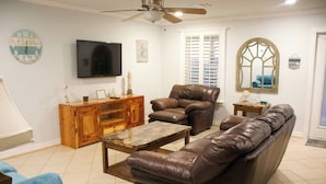 A living room with a brown leather sofa, a wooden cabinet, a television, and a ceiling fan.