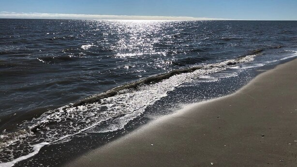 A beach with waves reaching the shore under a clear sky.