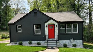 A two-story house with a red door, stone foundation, and a dark exterior. - NEW Decatur Bungalow - World Cup Ready Ready (Candler-McAfee)