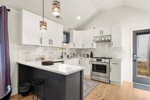 Una cocina moderna con armarios blancos, una isla central, electrodomésticos de acero inoxidable e iluminación colgante.