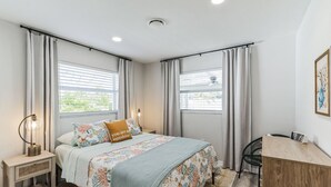 A bedroom with a bed, bedside table, chair, desk, and windows with curtains. - Coastal Comfort Getaway in the Heart of SRQ (Sarasota)