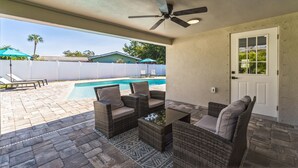 An outdoor patio with wicker furniture and a ceiling fan, overlooking a swimming pool. - Coastal Comfort Getaway in the Heart of SRQ (Sarasota)