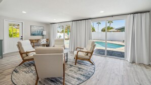 A spacious living room with a large window, a pool, and a view of palm trees. - Coastal Comfort Getaway in the Heart of SRQ (Sarasota)